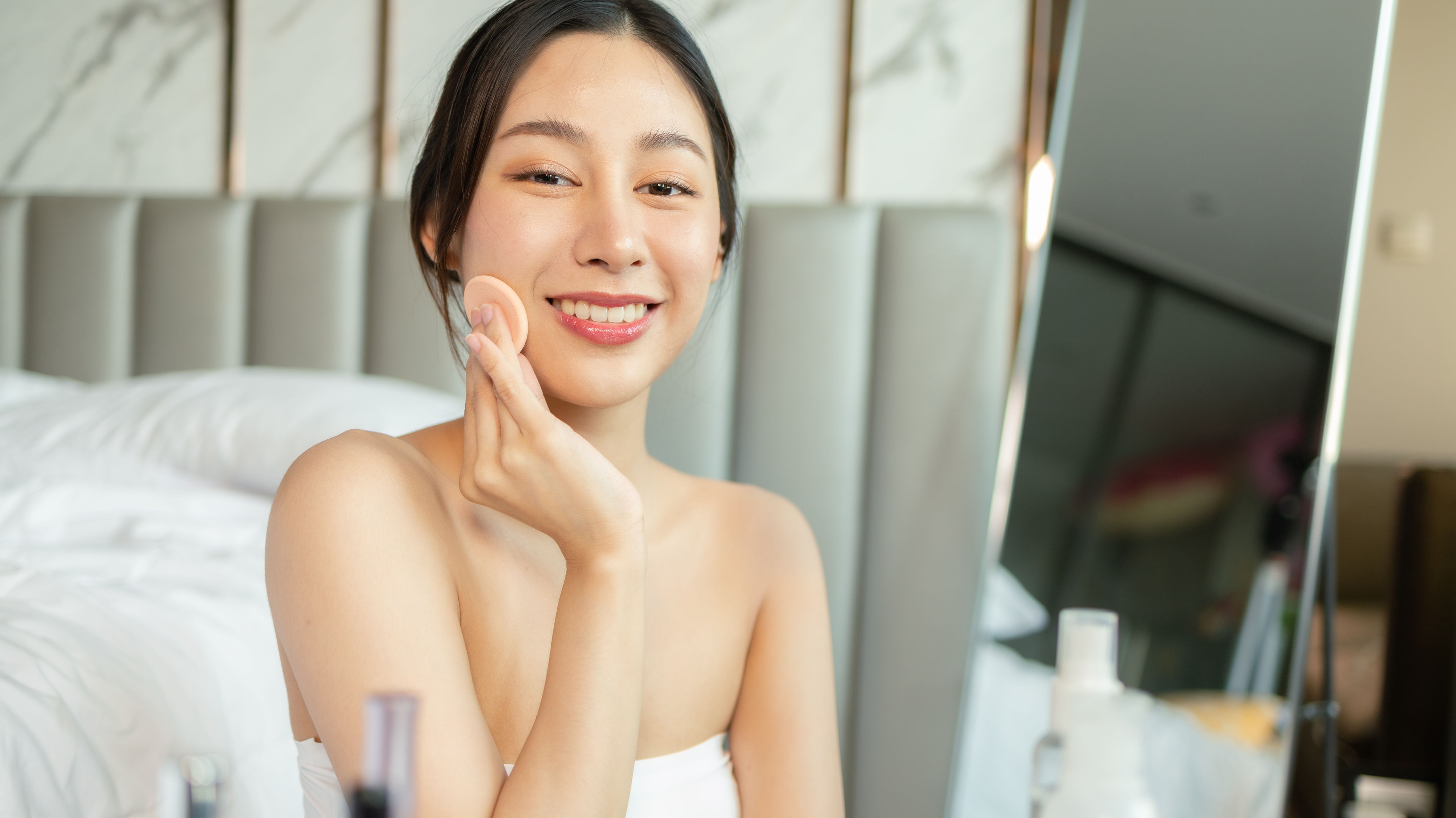 Smiling Woman Applying Makeup in Bedroom Setting